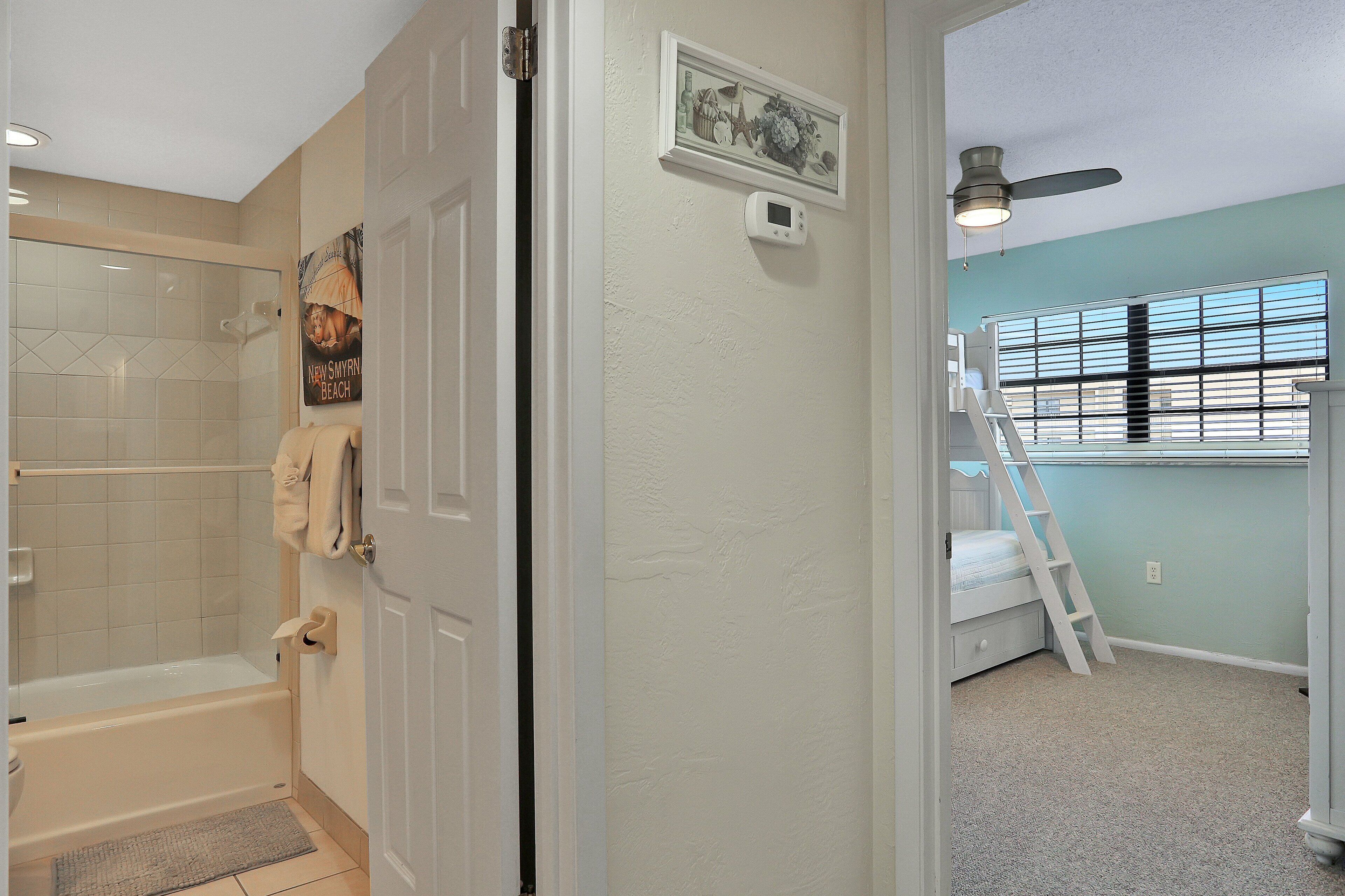 A bathroom with a shower, a toilet, and a towel rack. There is a door leading to another room.