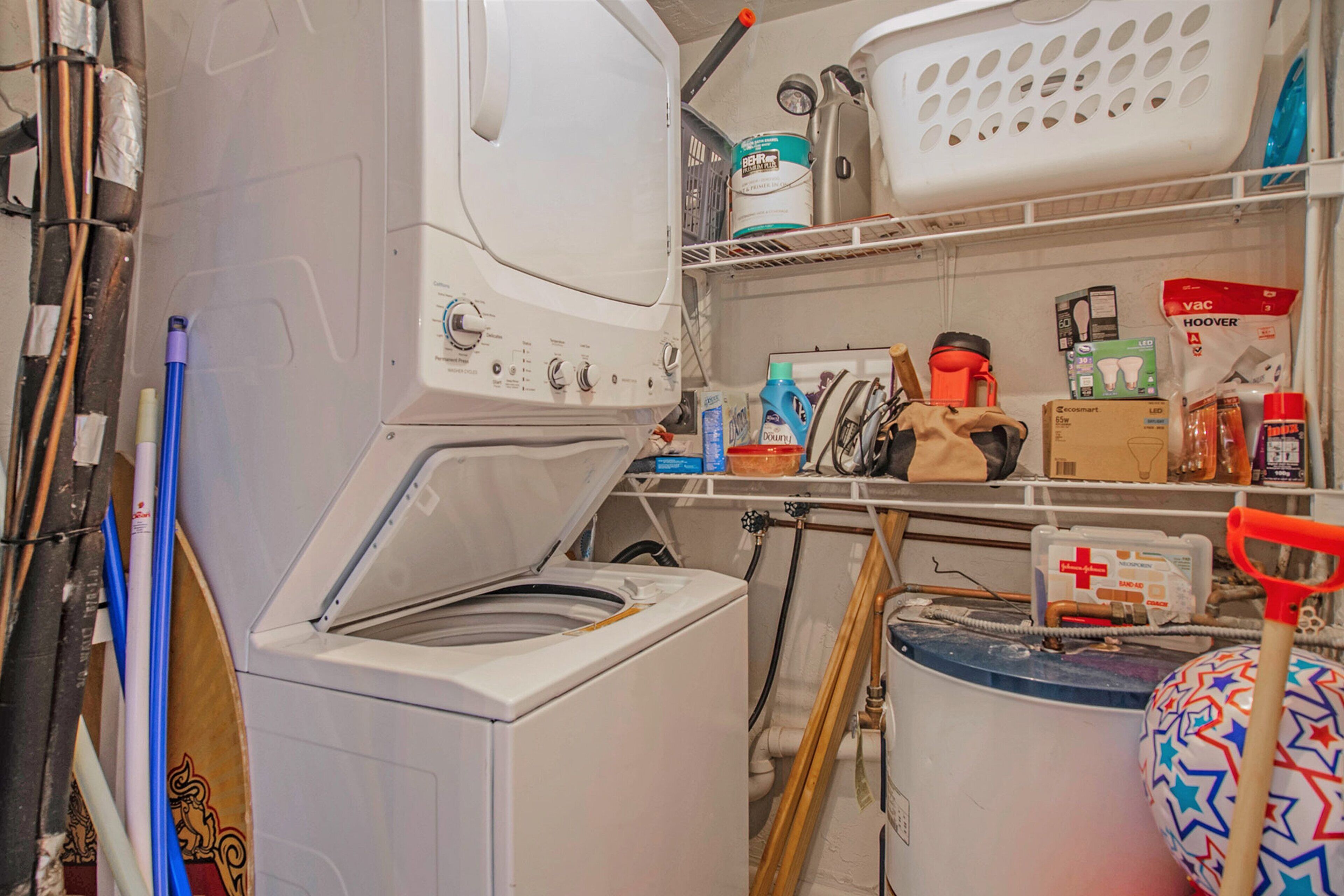 A laundry room with a washing machine, shelves with cleaning supplies, and a mop.