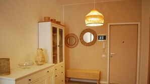 Una habitación con un armario blanco, una cesta de mimbre, un banco de mimbre y una lámpara colgante.