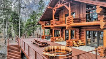 A log cabin with a deck, hot tub, and outdoor seating area.