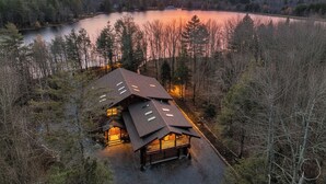 Een houten hut met schuin dak, omringd door bomen en een meer, tijdens zonsondergang.