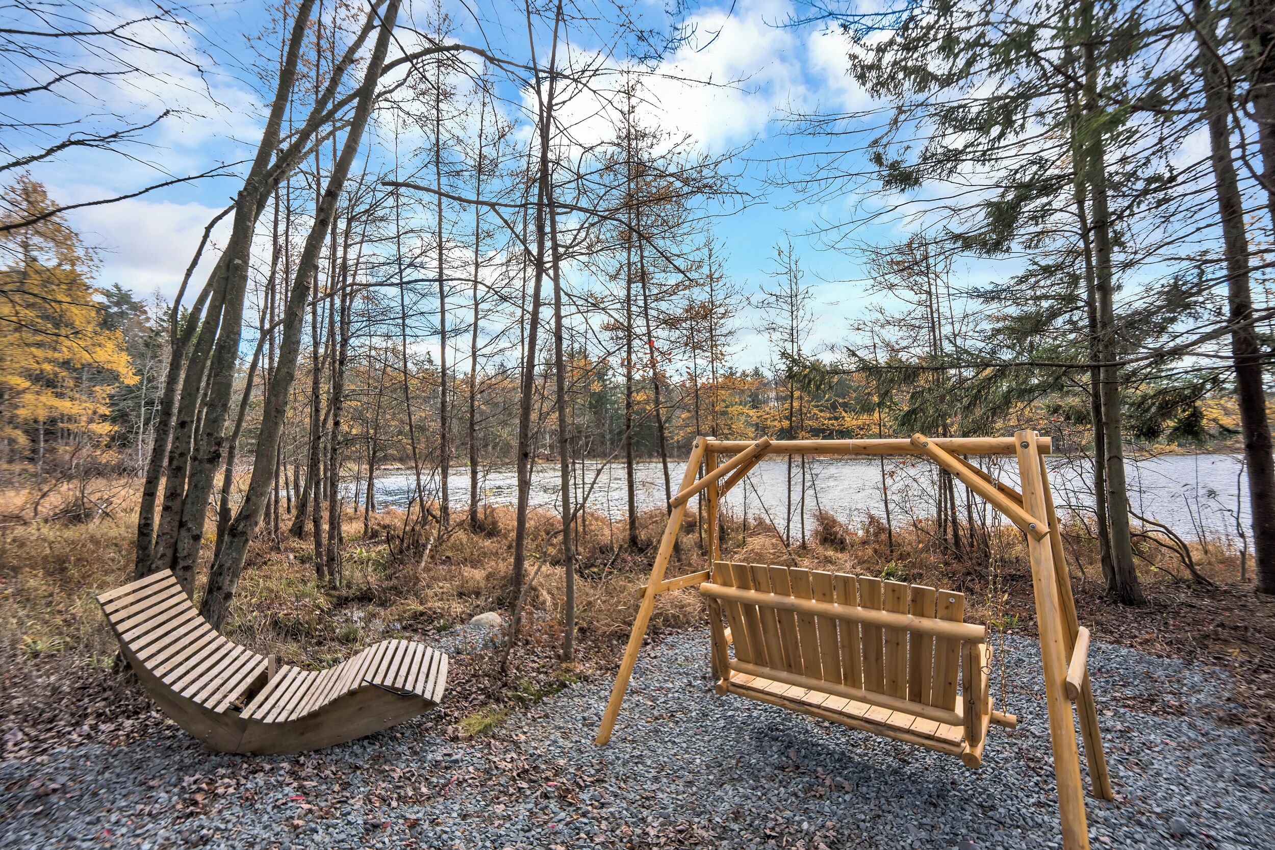Un ensemble de balançoires en bois et un banc incurvé, situés dans une zone boisée avec un lac en arrière-plan.