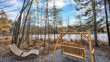 Un ensemble de balançoires en bois et un banc incurvé, situés dans une zone boisée avec un lac en arrière-plan.
