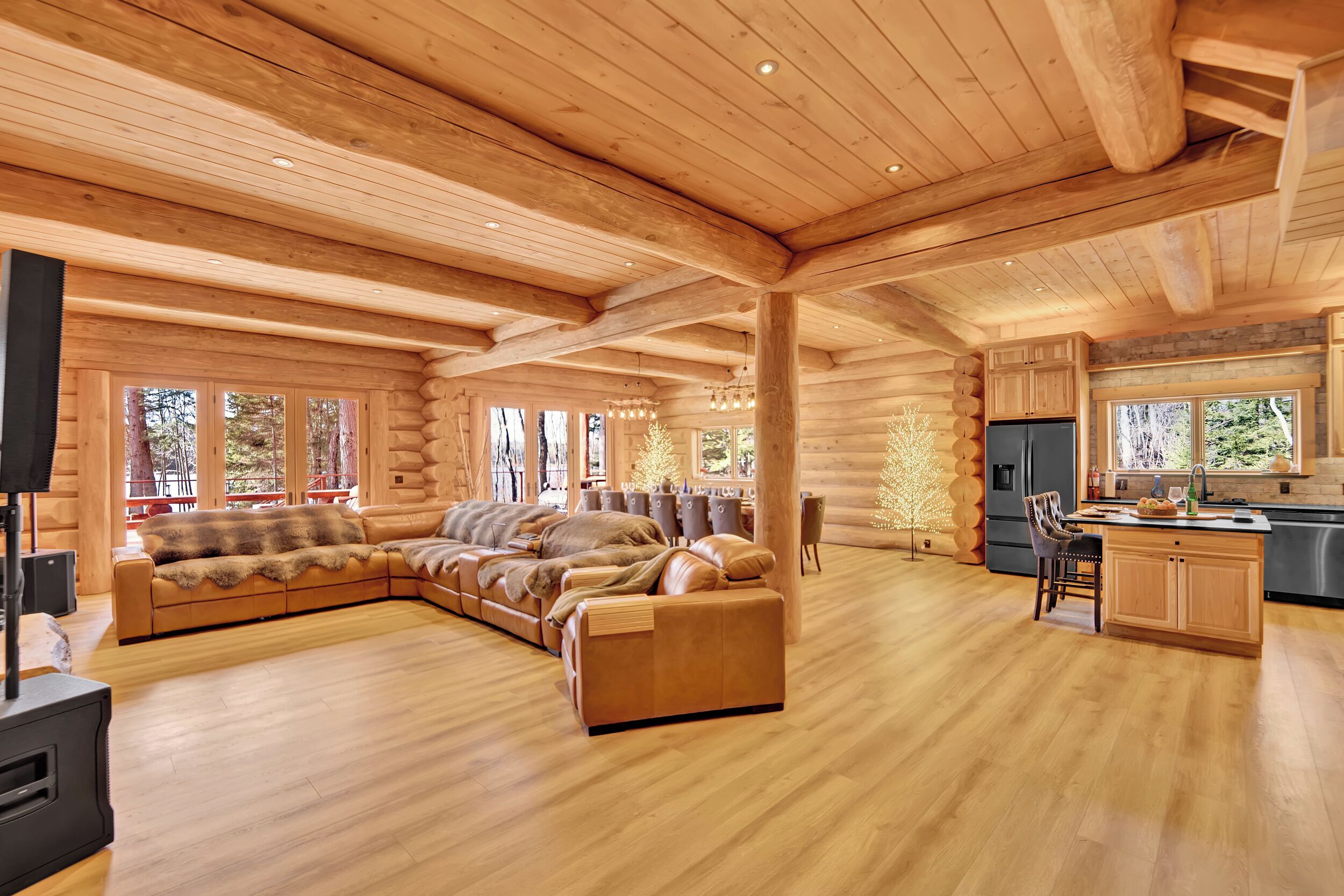 Een ruim houten blokhutinterieur met een grote hoekbank, een keukenhoek en een open haard.