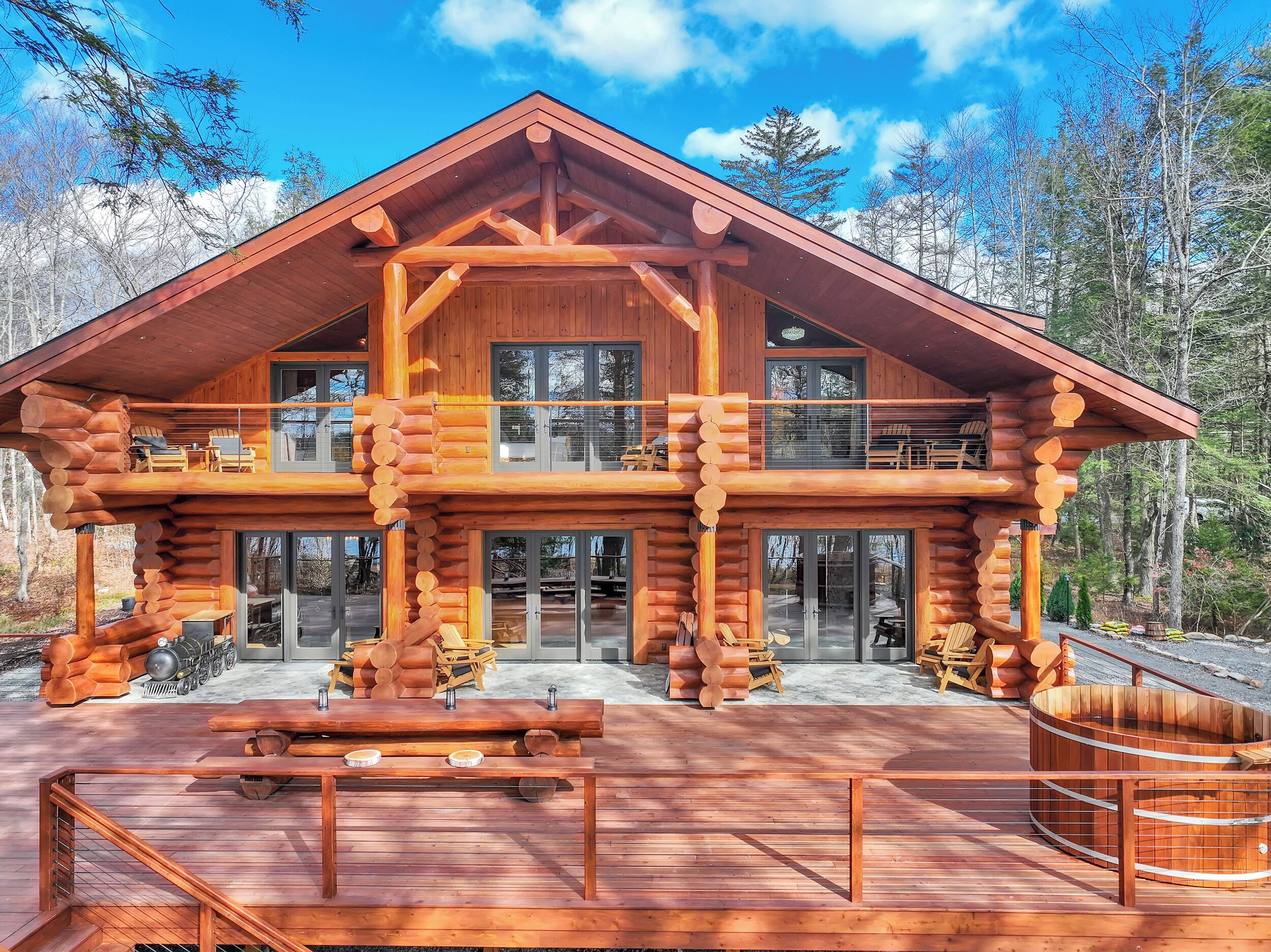 A log cabin with a spacious deck, multiple windows, and a prominent chimney.