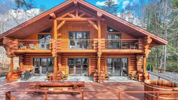 A log cabin with a spacious deck, multiple windows, and a prominent chimney.