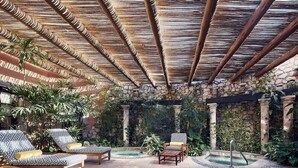 Un espacio al aire libre cubierto con sillones de descanso, una piscina pequeña y un muro de piedra con vegetación.