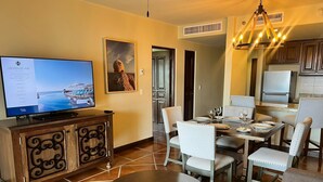 Un comedor con una mesa redonda, sillas, un televisor y una cocina al fondo.