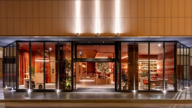 En moderne hotelindgang med glasdøre, siddepladser indendørs og varm belysning.