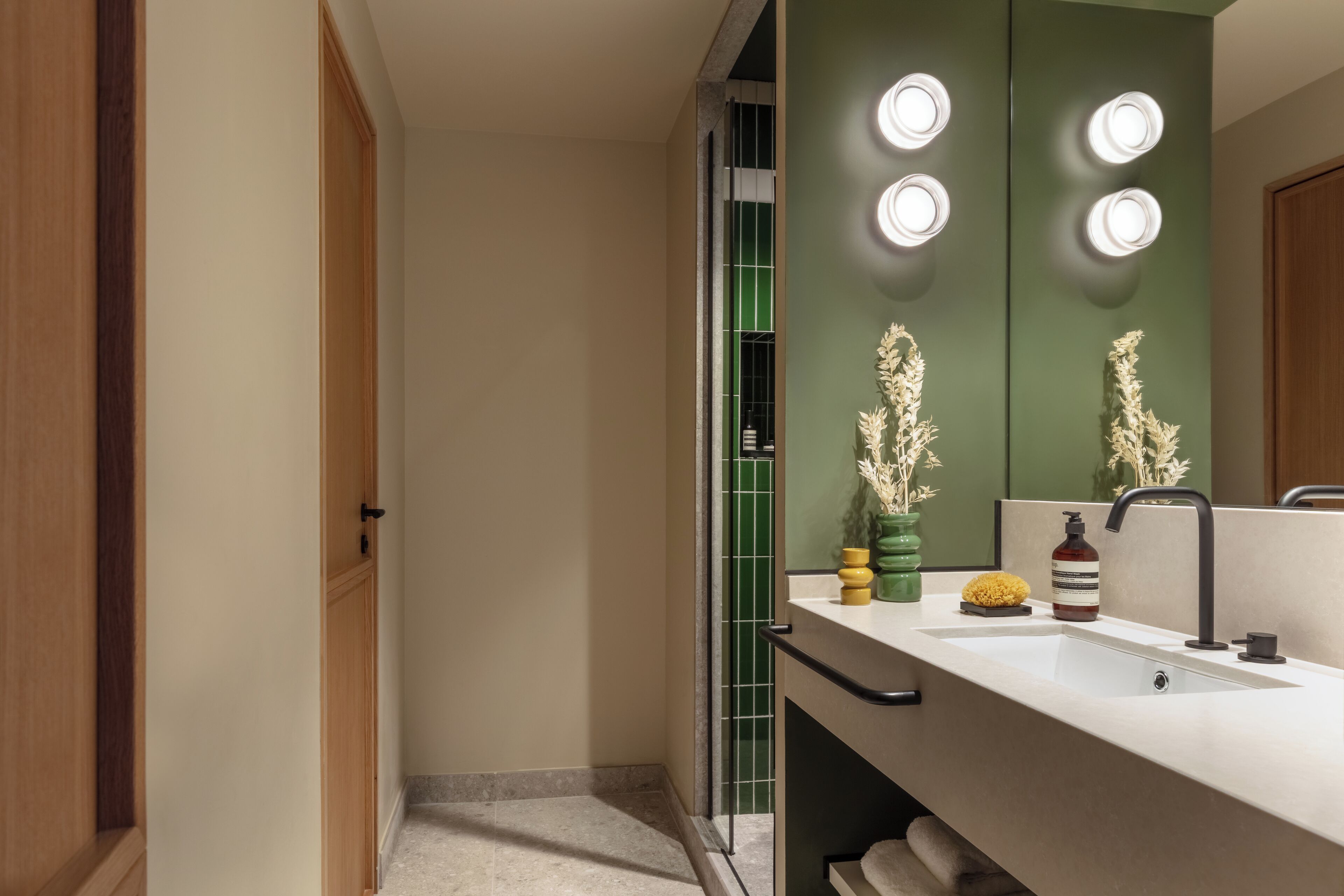 Un baño moderno con un espejo grande, un lavabo y tocador. Hay tres luces encima del espejo y un perchero debajo.