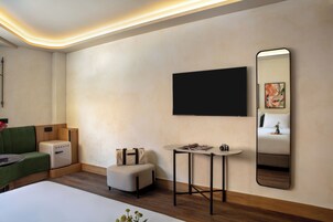 A modern hotel room with a flat-screen TV, a small round table with a chair, a sofa, a bed, and a large mirror.