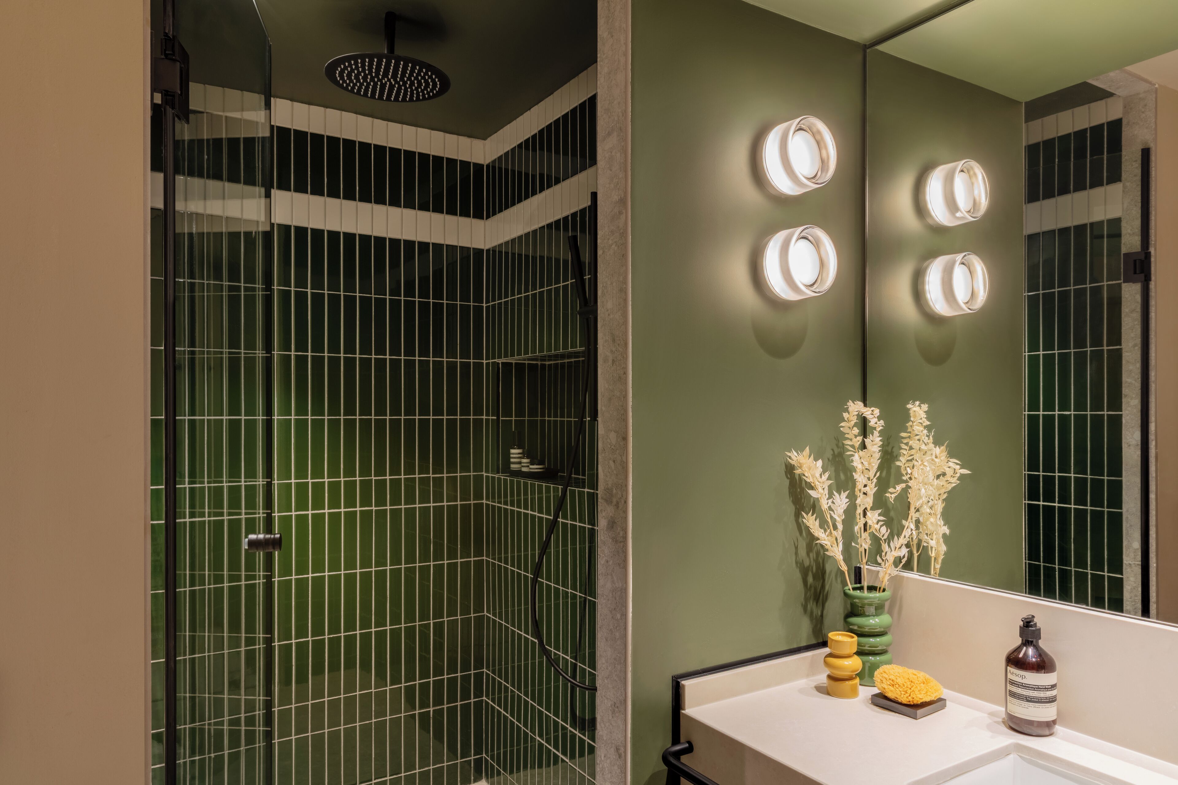 A modern bathroom with a shower area, a vanity with a mirror, and a vase with dried flowers.