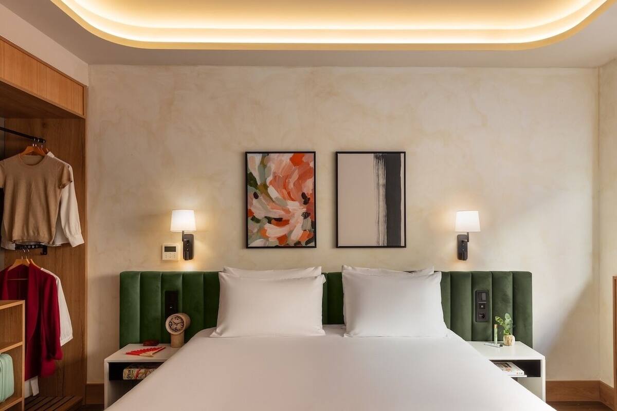 A hotel room with a bed, green headboard, bedside tables, a clock, and two wall-mounted lamps.