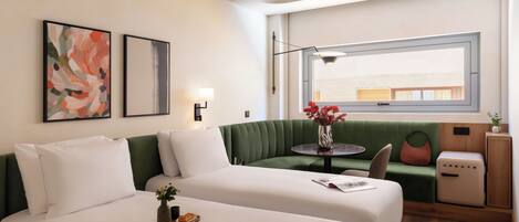 A modern hotel room with two beds, a green sofa, a small table with a vase, and a window with a view.