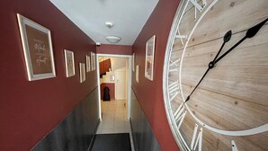 Un corridoio con un grande orologio di legno sulla destra, quadri appesi alle pareti e una porta in fondo.
