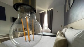 Una camera d'albergo con un letto, un comodino, una lampada e una finestra con tende.