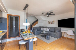 A modern kitchen with a dining area, a gray sofa, a TV, and a ceiling fan. - Arizona's Bay Holiday Home with Sea Views, Hot Tub, and Private Terrace (Mogán)