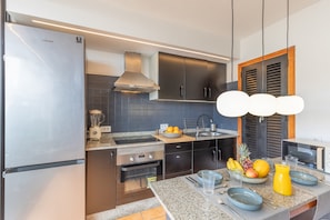 A modern kitchen with stainless steel appliances, a granite countertop, and a fruit bowl on the island. - Arizona's Bay Holiday Home with Sea Views, Hot Tub, and Private Terrace (Mogán)