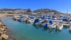 A marina with numerous boats docked, a rocky shoreline, and buildings in the background. - Arizona's Bay Holiday Home with Sea Views, Hot Tub, and Private Terrace (Mogán)