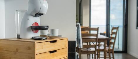A modern kitchen with a coffee machine on a wooden cabinet, a glass container, and a cup.