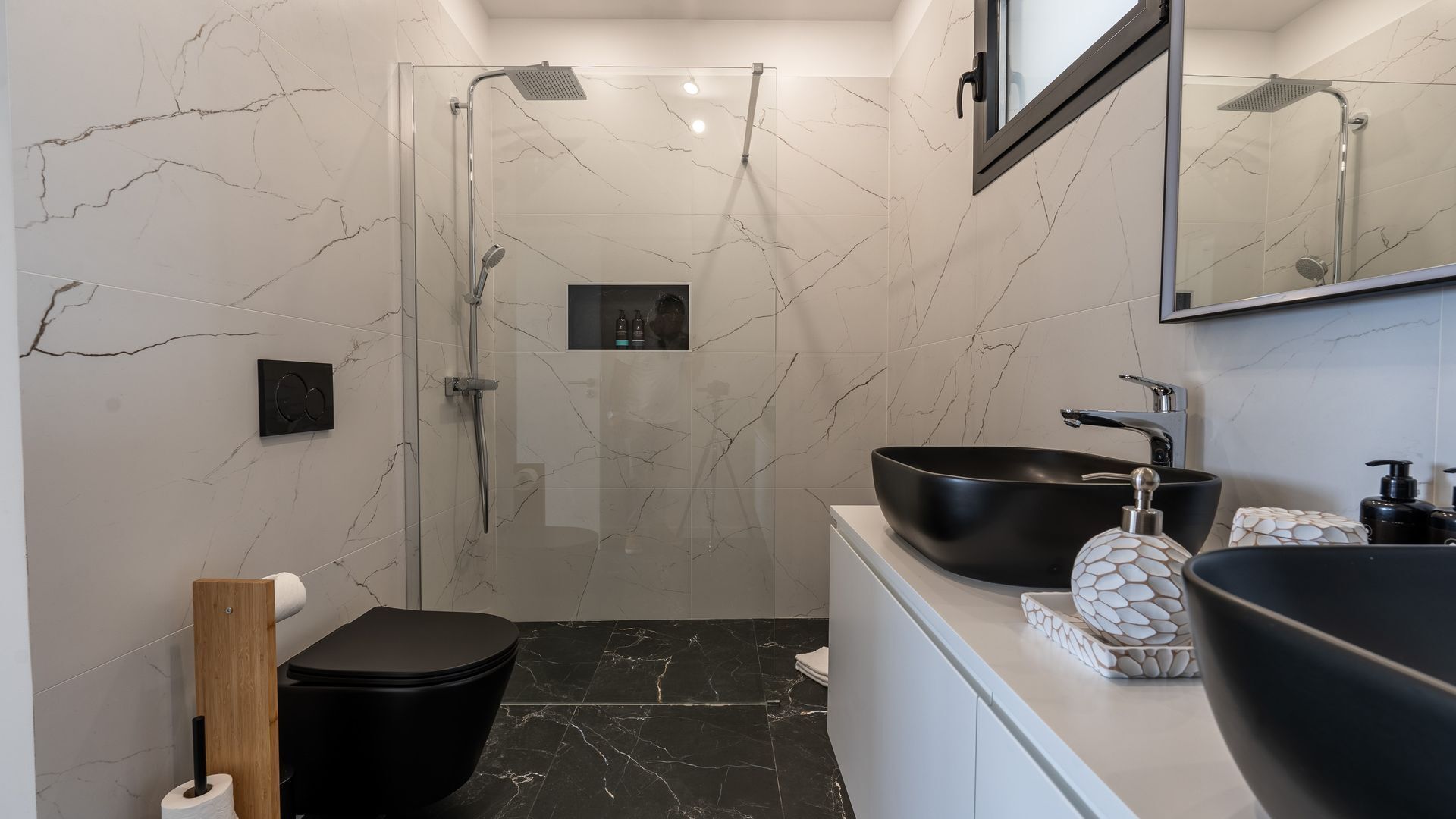 Ein modernes Badezimmer mit einer gläsernen Duschkabine, einem schwarzen Waschbecken und einem marmorbelagten Boden.