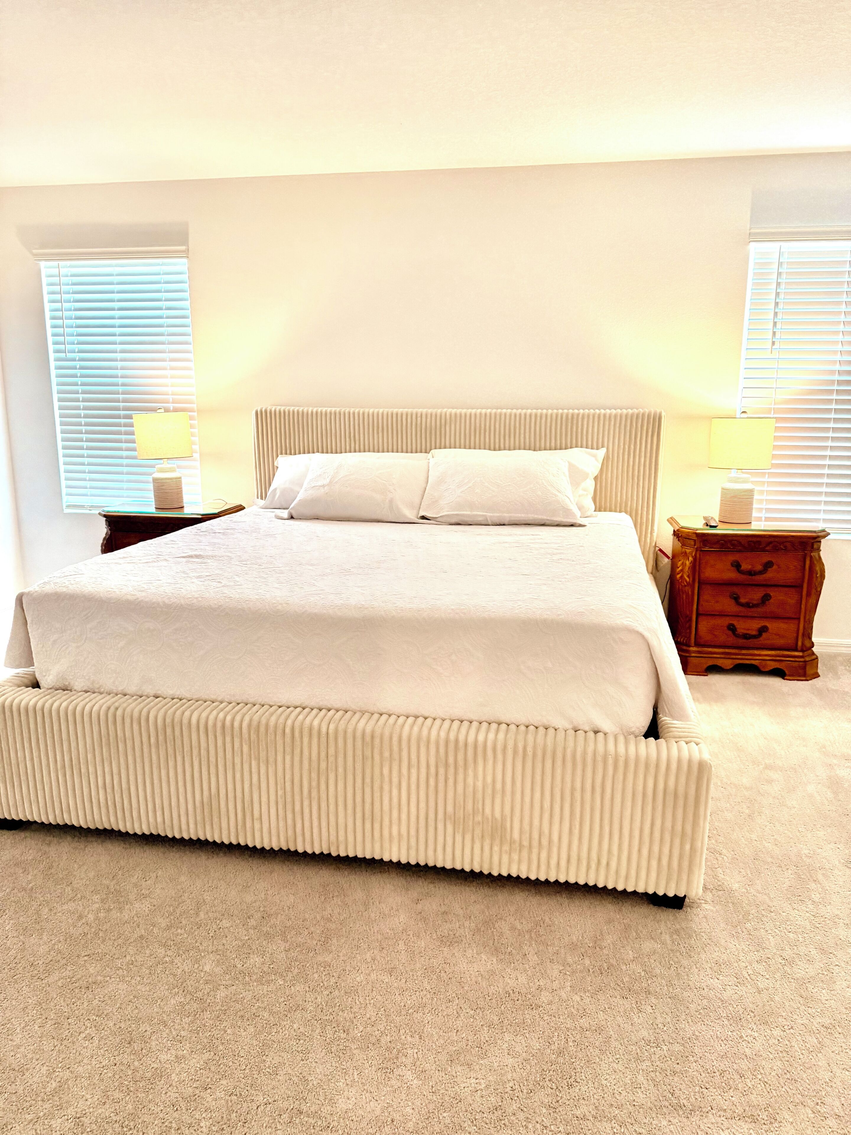 A neatly made bed with a white comforter and pillows, a bedside table with a lamp, and a wooden nightstand with drawers.
