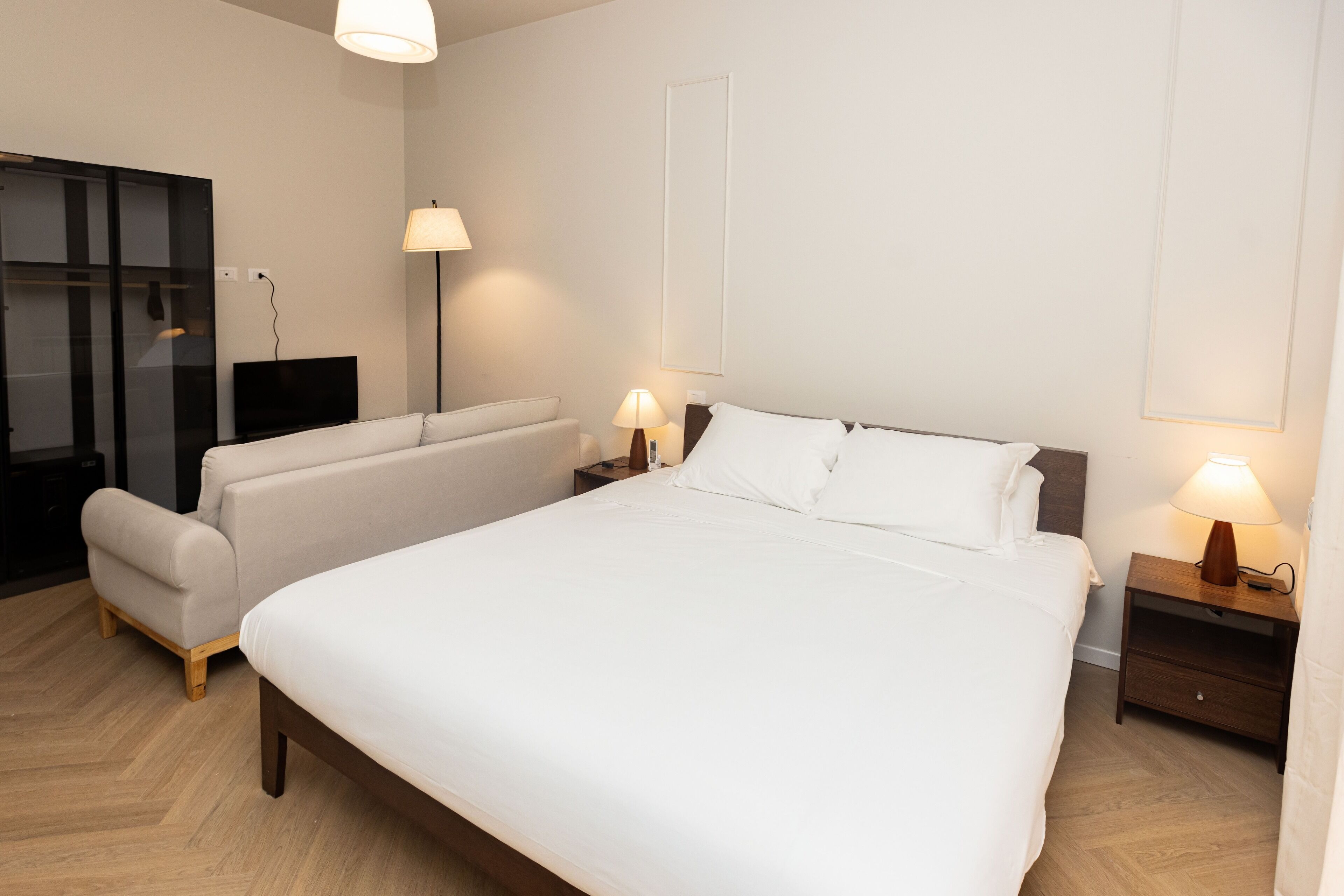 Une chambre d’hôtel moderne avec un grand lit, un canapé, une télévision et deux lampes de chevet.