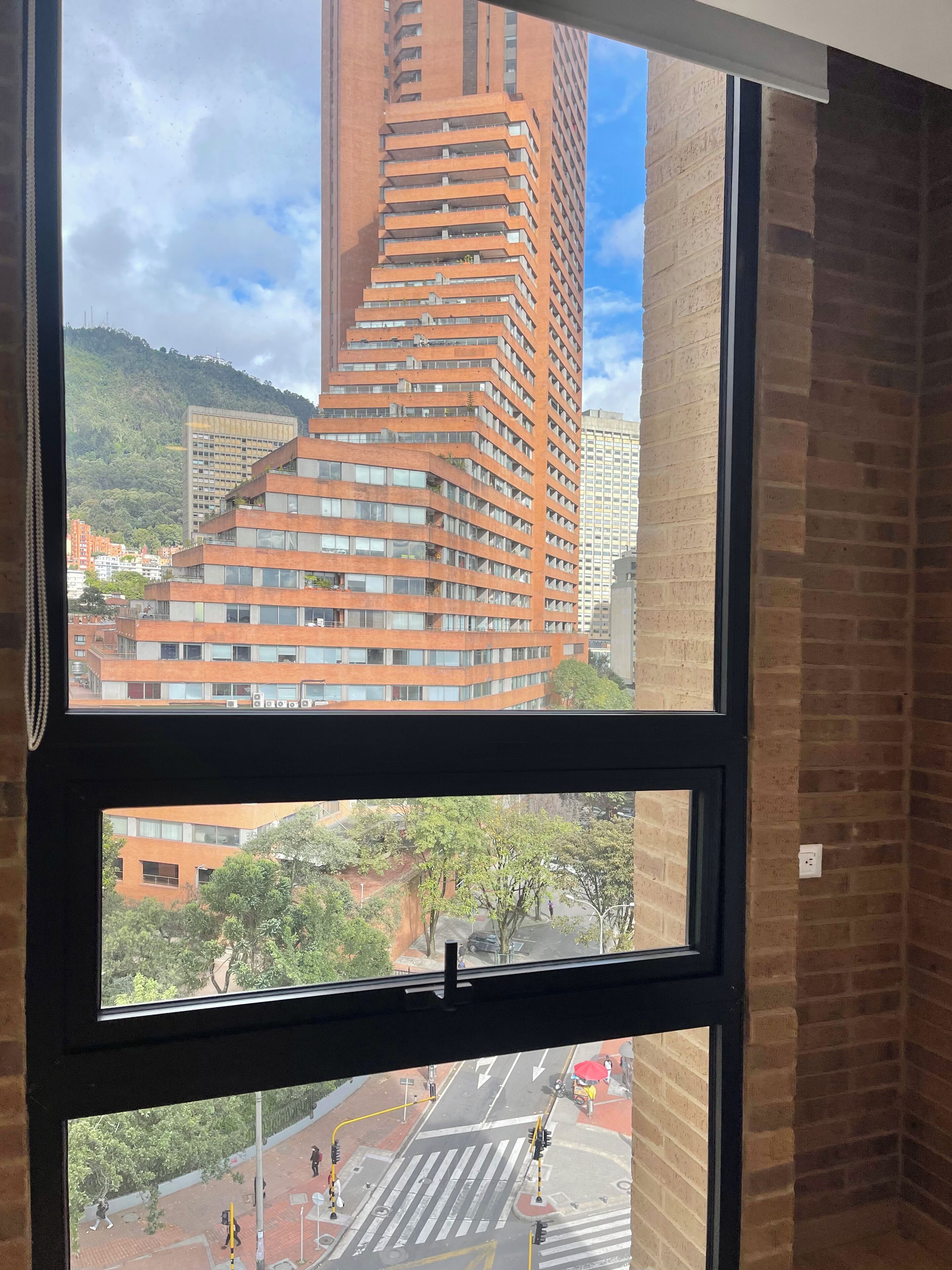 A view through a window of a multi-story building with a unique angular design, a brick wall, and a street scene below.