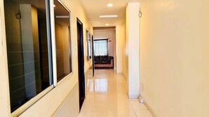 A corridor with a sofa at the end, a window with blinds, and a door on the left. - Hotel Star 21 (Indore)