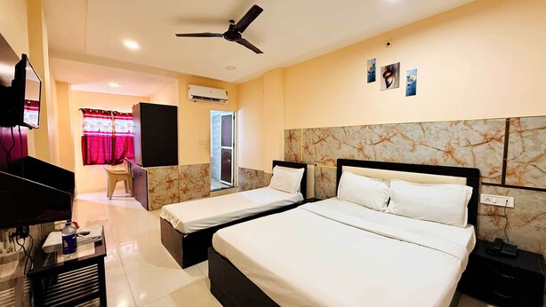A hotel room with two beds, a ceiling fan, an air conditioning unit, a TV, a desk with a chair, and a bathroom with a shower curtain. - Hotel Star 21 (Indore)