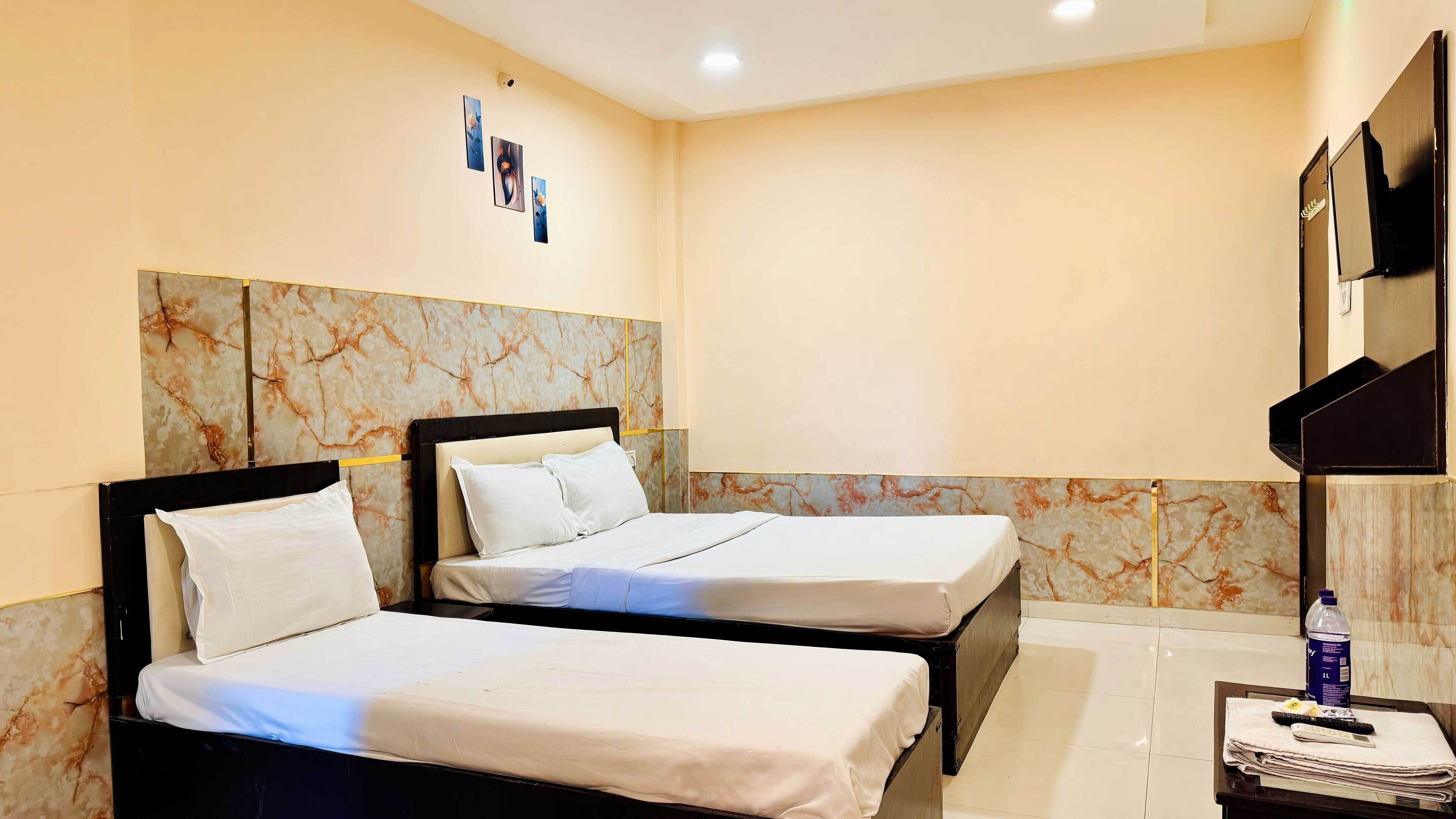 A hotel room with two beds, a marble headboard, a flat-screen TV, and a small table with a bottle and remote controls.