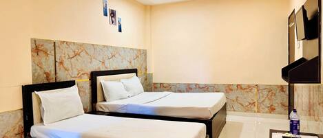 A hotel room with two beds, a marble headboard, a flat-screen TV, and a small table with a bottle and remote controls.