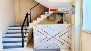 A hotel reception area with a marble reception desk, a staircase with black railings, and a 'Check In/Check Out' sign. - Hotel Star 21 (Indore)