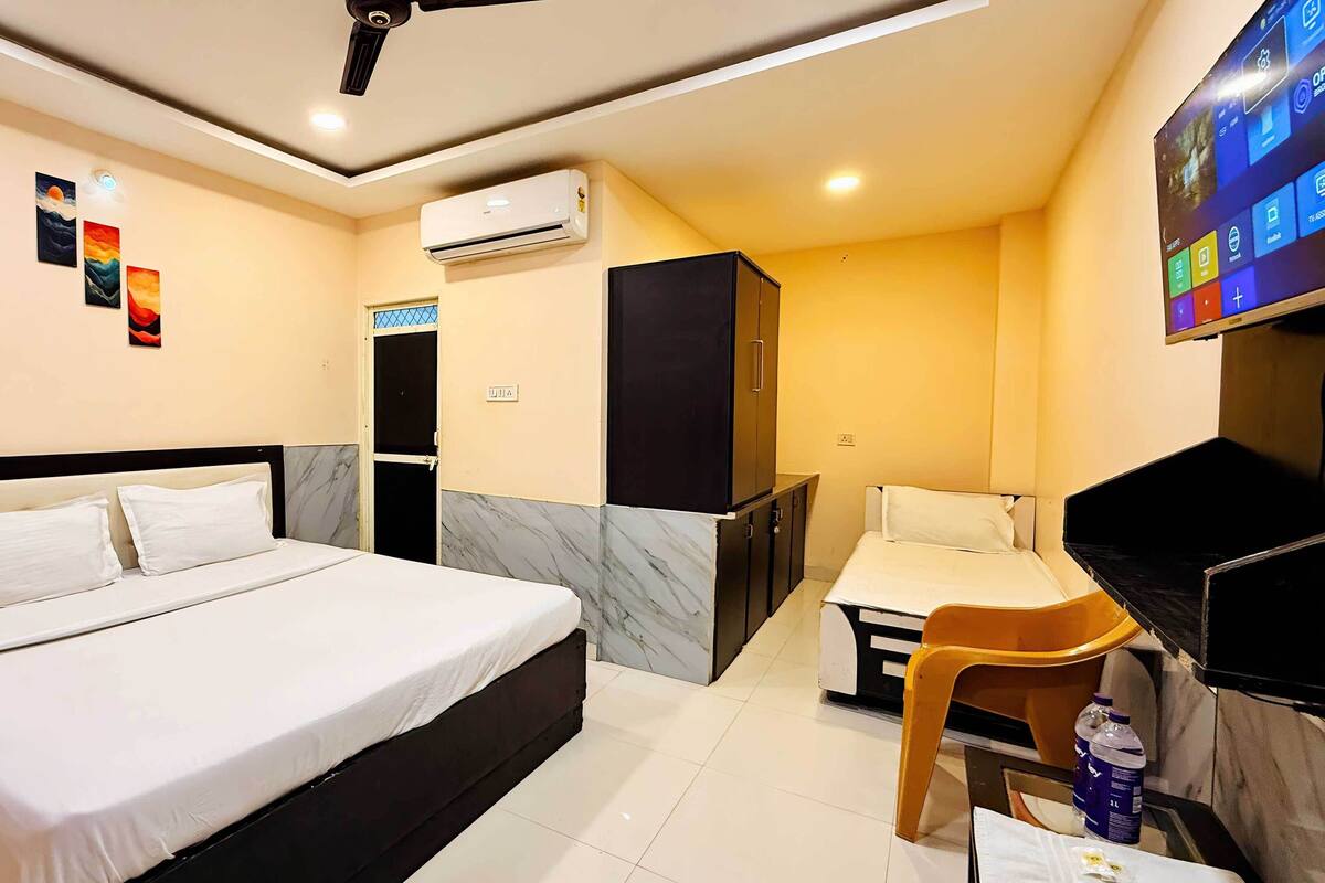 A hotel room with a bed, a desk, a chair, an air conditioning unit, and a TV.