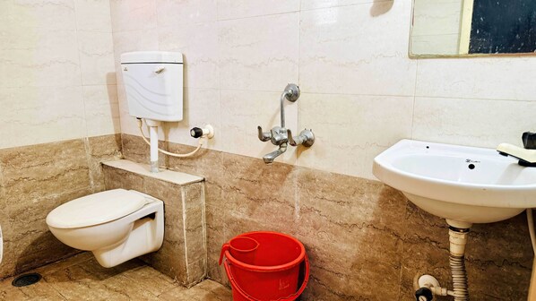 A bathroom with a toilet, a red bucket, a sink, and a shower control. - Hotel Star 21 (Indore)