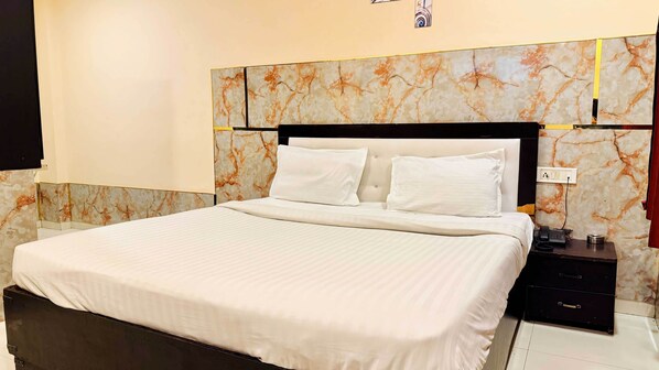 A neatly made bed with white linens, a marble-patterned headboard, and a bedside table with a phone and a small lamp. - Hotel Star 21 (Indore)