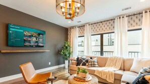 A modern living room with a flat-screen TV displaying a streaming service menu, a sofa, a coffee table, and a large window with patterned curtains. - 8 Minutes To Downtown Nashville Wifi And Workspace (Nashville)