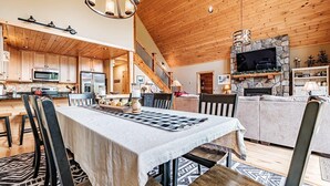 Ein großzügiger Wohnbereich mit hohen Decken, Holzbalken, einem Kamin aus Stein und einer Küche mit modernen Geräten.