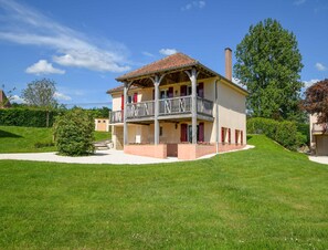Ein zweistöckiges Haus mit Balkon, umgeben von einem gepflegten Rasen und Bäumen.