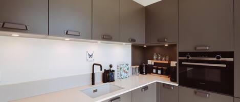 A modern kitchen with grey cabinets, a white countertop, and a built-in oven.
