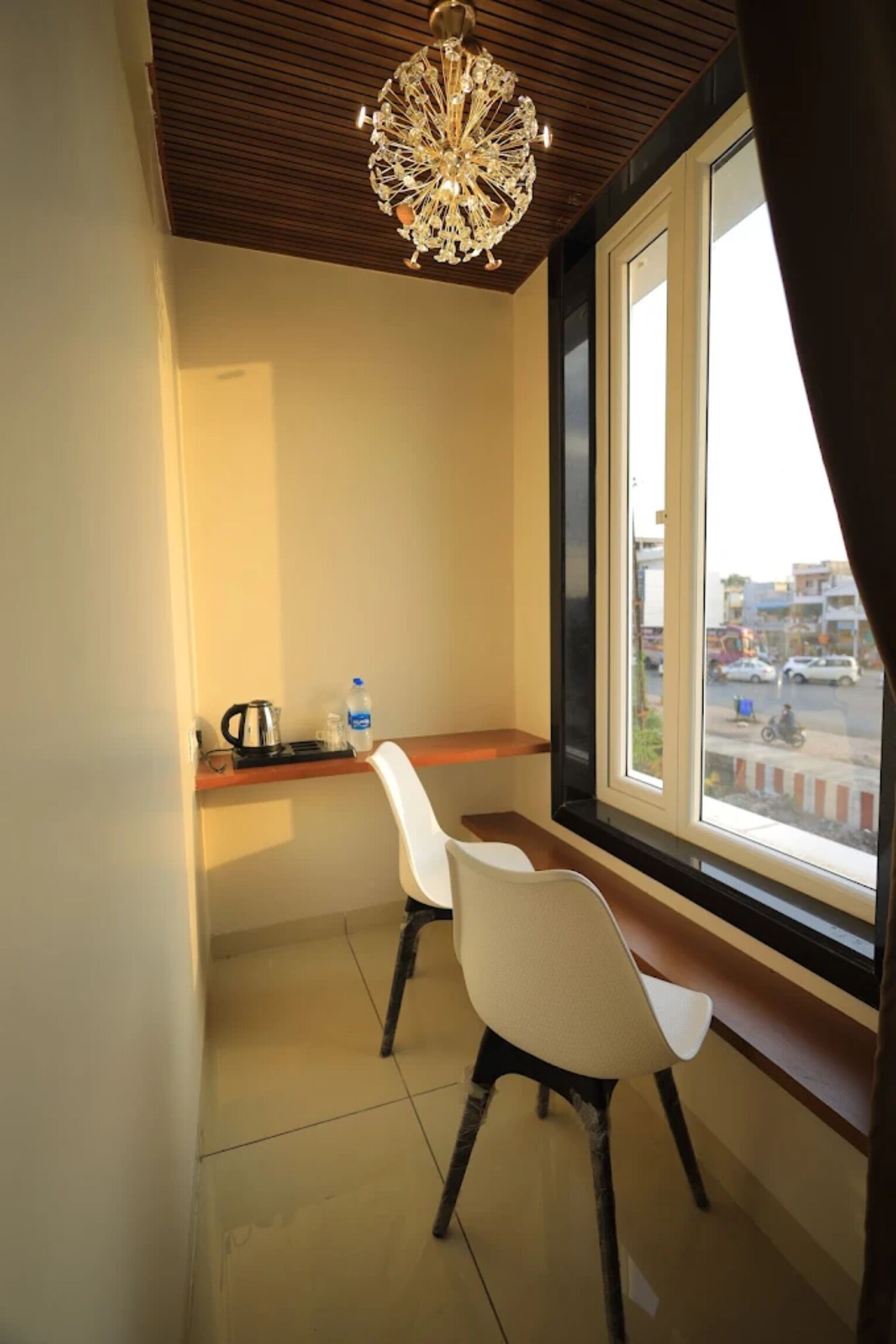 A small balcony with two white chairs, a table, a kettle, and a bottle of water.