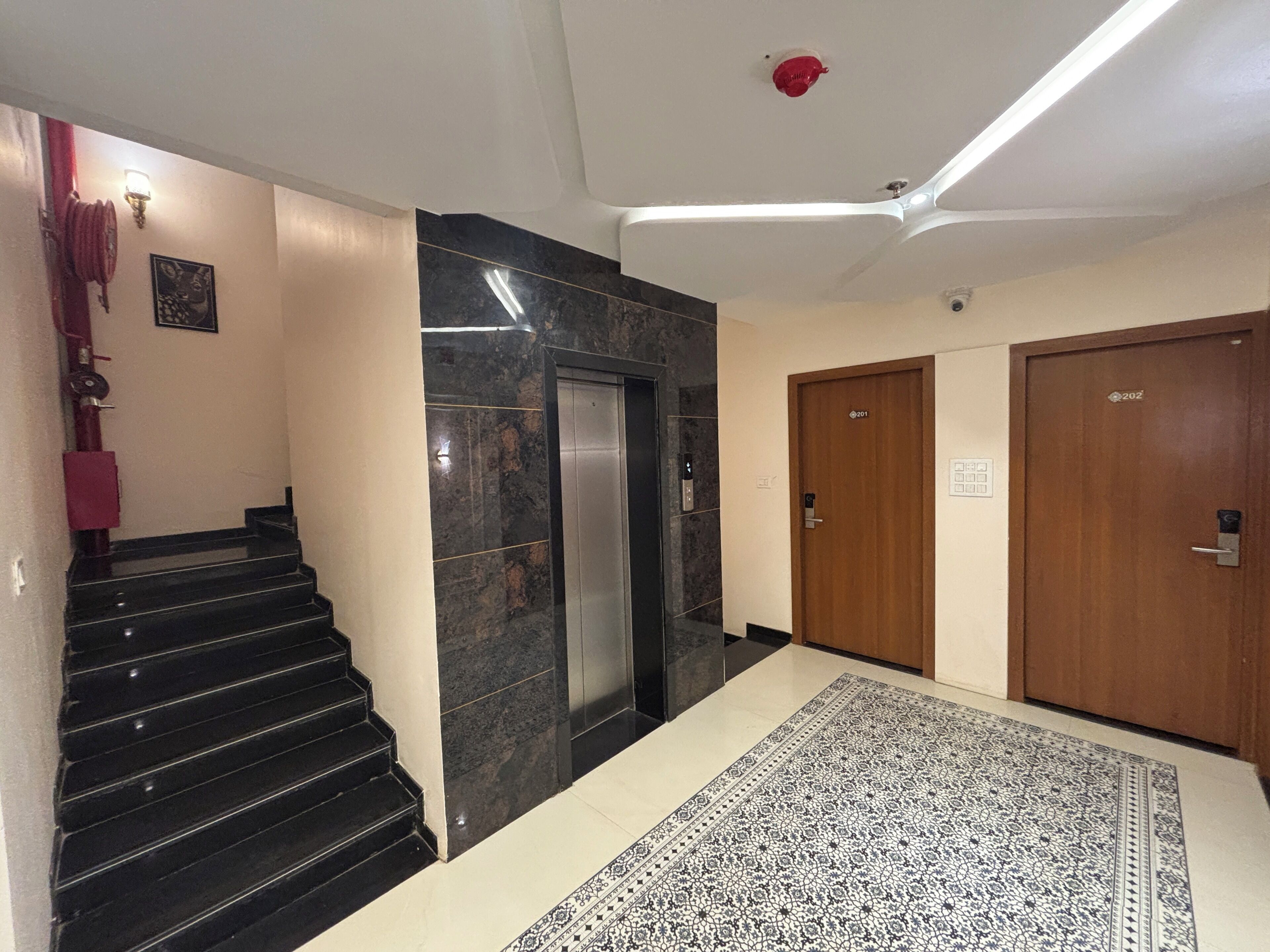 A hotel lobby with a marble staircase, an elevator, and a patterned carpet.