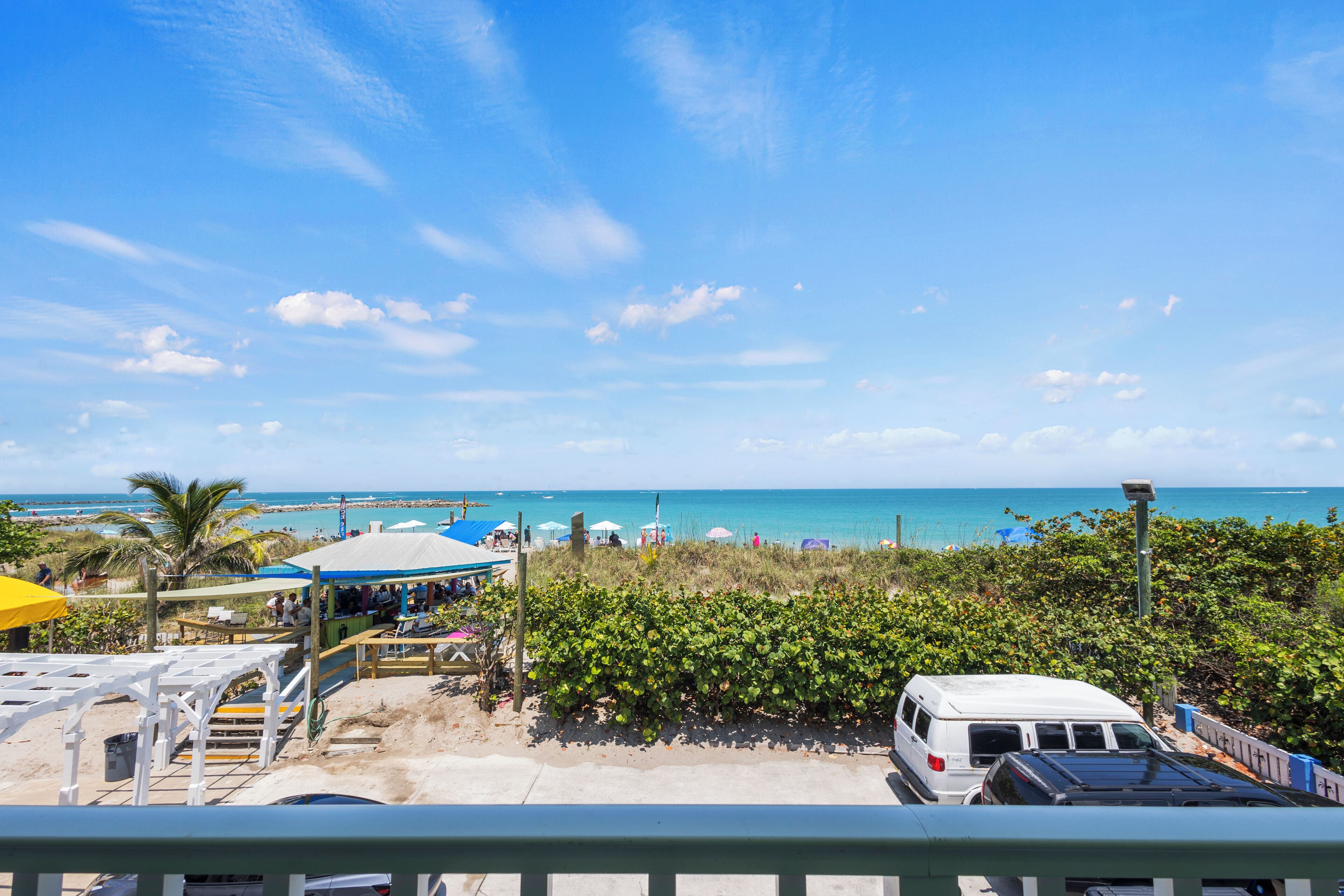 A beachside view with a white van, beach umbrellas, and a clear blue sky.