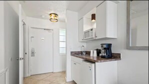 A compact kitchen with white cabinets, a microwave, a coffee maker, and a trash bin. - Oceanfront Inn Room #5 - Standard Room - King Bed (Fort Pierce)