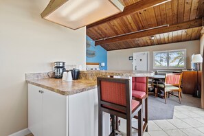 A kitchen with a wooden ceiling, a coffee maker, and a dining area with chairs and a table. - Oceanfront Inn Suite #12- Ocean View Balcony - King Bed (Fort Pierce)