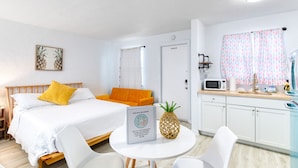 Ein Hotelzimmer mit einem Bett, einem kleinen Tisch mit einer Ananas, einer Mikrowelle und einer Küchenzeile.