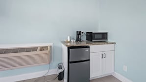 A compact kitchenette with a built-in air conditioner, a refrigerator, a microwave, and a coffee maker on a granite countertop. - Oceanfront Inn Room #1 - Partial Ocean View, King Bed (Fort Pierce)