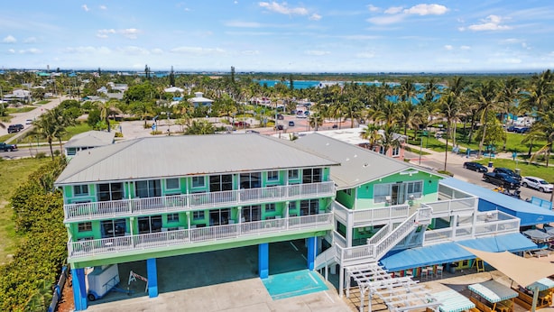 Un hôtel à plusieurs étages doté d’un balcon au rez-de-chaussée, d’un espace piscine et offrant une vue sur les environs, notamment sur les palmiers et la plage.