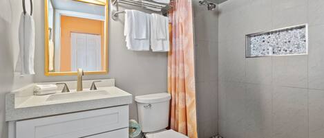 A bathroom with a sink, mirror, toilet, and shower area.