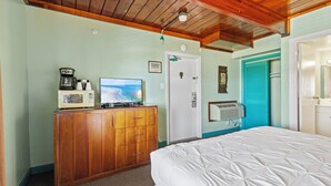 A bedroom with a wooden dresser, a bed, a television, and a door with a blue shutter. - Oceanfront Inn Room #7 - Partial Ocean View - King Bed (Fort Pierce)